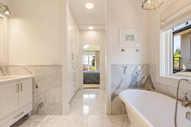 A bright, elegant bathroom with marble tile walls and floors, a freestanding tub, and large windows - 1248 Kings Avenue, West Vancouver