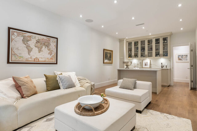 A bright living room with hardwood floors, a white sofa, and a kitchenette in the background - 1248 Kings Avenue, West Vancouver