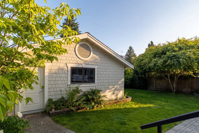 A bright exterior shot of a white brick house with small windows, a well-maintained lawn, and garden planters. - 1248 Kings Avenue, West Vancouver