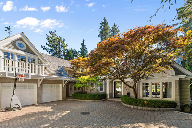 The building exterior shows a brick driveway, white railings on the upper level, garage doors, and an autumn-colored tree in 