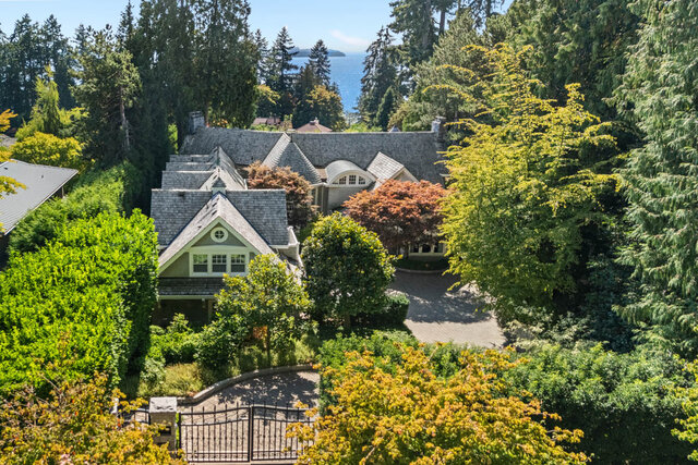 The building exterior shows a house with a shingled roof, surrounded by mature trees and a gated driveway - 2940 Mathers Avenue, West Vancouver