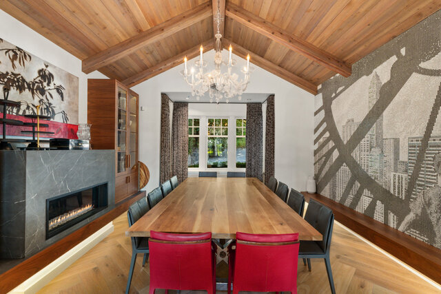 The dining area features a large wooden table, red and black chairs, a chandelier, a fireplace, and large windows.