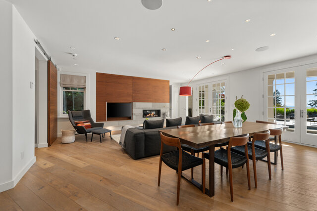 The dining area features a wooden table with chairs, hardwood floors, and a view of the living room with a fireplace and larg