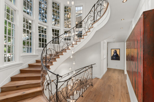 The hallway features a wooden staircase with wrought iron railing, floor-to-ceiling windows, hardwood floors, and artwork on 