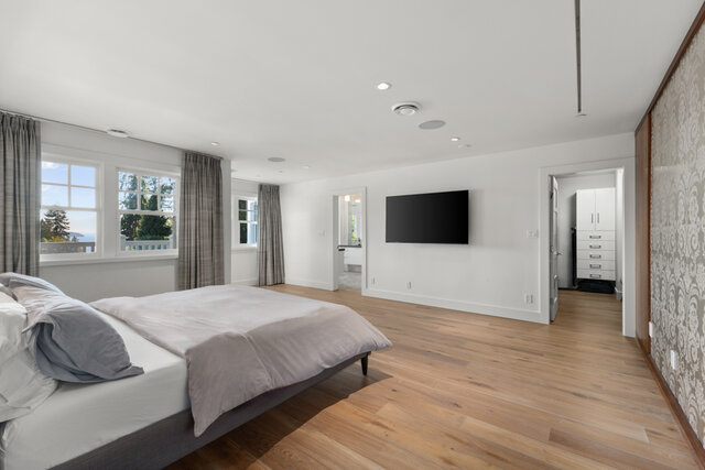 This is a bedroom with a bed, large windows, hardwood floors, and a wall-mounted TV. - 2940 Mathers Avenue, West Vancouver