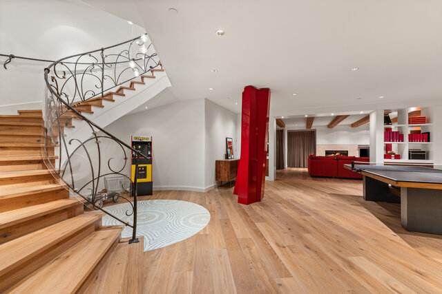 The lounge features hardwood floors, a pool table, a red sofa, and a spiral staircase with a wrought iron railing.