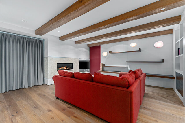 The living room features a red sofa, a fireplace, exposed wooden ceiling beams, and built-in wall shelves. - 2940 Mathers Avenue, West Vancouver
