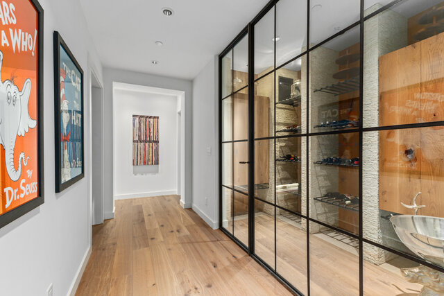 A hallway with hardwood floors, framed artwork on the walls, and glass-enclosed storage with black metal frames - 2940 Mathers Avenue, West Vancouver