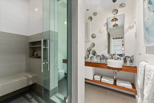 Bathroom with glass shower enclosure, built-in tile bench, wooden vanity, and folded towels on a shelf - 2940 Mathers Avenue, West Vancouver