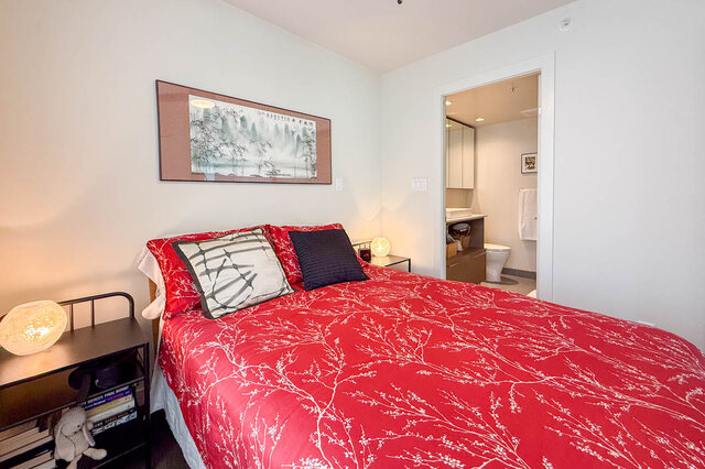 Cozy bedroom with red branch-patterned bedding and framed landscape art above the bed. - 505-189 Keefer Street, Vancouver Downtown