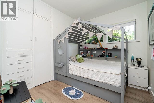 This is a bedroom with a bed, built-in shelves, a window, wood flooring, and a small rug. - 2784 Crescentview Drive, North Vancouver