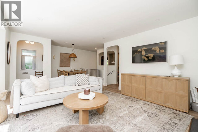 The living room features a white sofa, round coffee table, patterned rug, wooden sideboard, and large wall art.