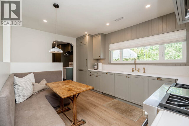 The kitchen has light-colored cabinets, a window with a view, a brass faucet, a wooden table, and hardwood floors.