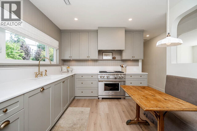 The kitchen has light gray cabinets, a stainless steel stove, white countertops, a window with an outdoor view, and wood floo