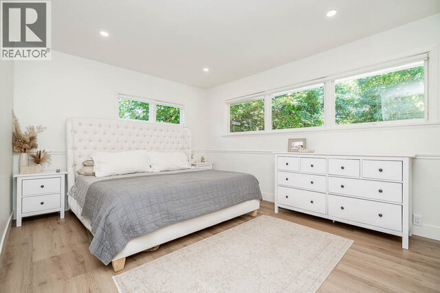 This is a bedroom with a bed, dresser, two nightstands, large windows, and hardwood floors. - 2784 Crescentview Drive, North Vancouver