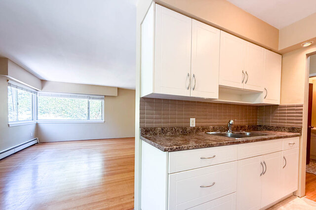 The kitchen has white cabinets, a granite countertop, a tile backsplash, a stainless steel sink, and hardwood floors.