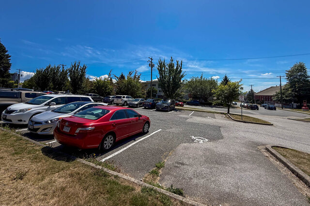 The building exterior shows a paved parking lot with parked cars and a handicap parking symbol. - 102-461 16th West street, North Vancouver