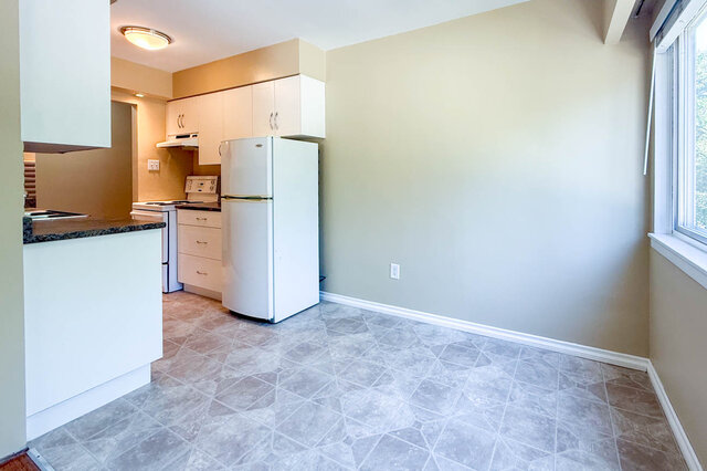 The kitchen has white cabinets, a refrigerator, a stove, a dark countertop, and a window. - 102-461 16th West street, North Vancouver