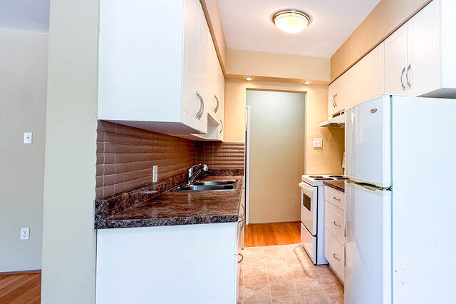 The kitchen has white cabinets, granite countertops, a sink, a refrigerator, and a stove. - 102-461 16th West street, North Vancouver
