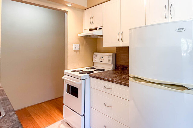 The kitchen has white cabinets, a white stove, a white refrigerator, a granite countertop, and hardwood floors.