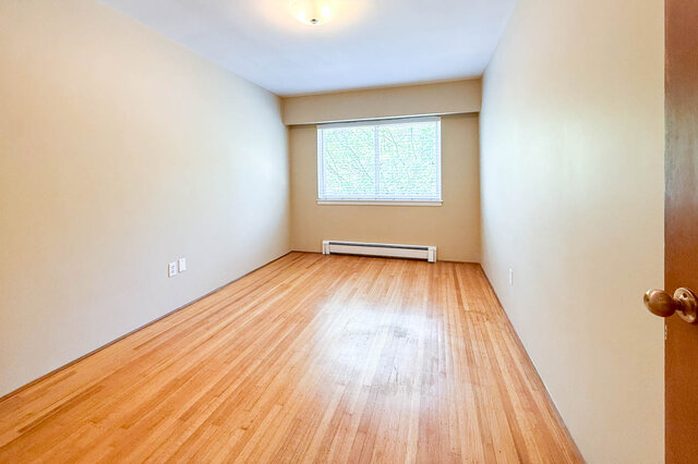 This is a bedroom with hardwood floors, a window, and a baseboard heater. - 102-461 16th West street, North Vancouver