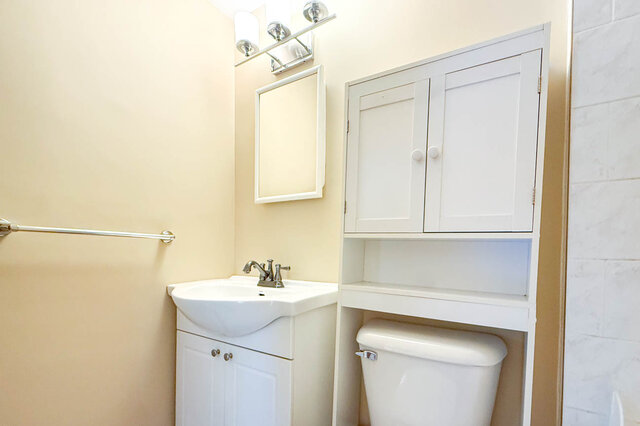 This is a bathroom with a white sink vanity, a toilet, a wall-mounted mirror, and a towel bar. - 102-461 16th West street, North Vancouver