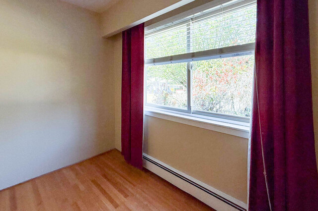 This is a bedroom with hardwood floors, a window with blinds, and purple curtains. - 102-461 16th West street, North Vancouver