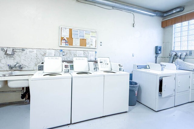 The laundry room contains multiple washing machines, dryers, a sink, and a bulletin board on the wall. - 102-461 16th West street, North Vancouver