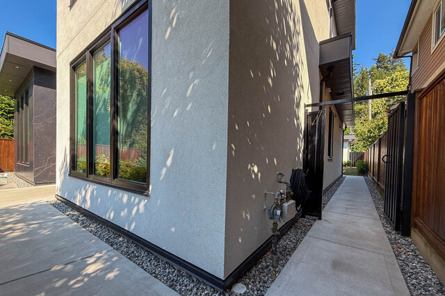 Exterior side walkway with a large dark-framed window, concrete path, and black metal gate. - Suite-1384 Hope Road, North Vancouver