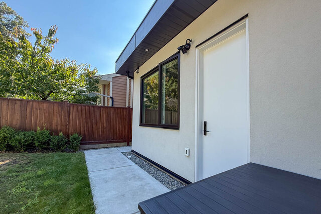 Private side entry with white door, dark-framed window, and concrete path bordered by gravel and a wooden fence.