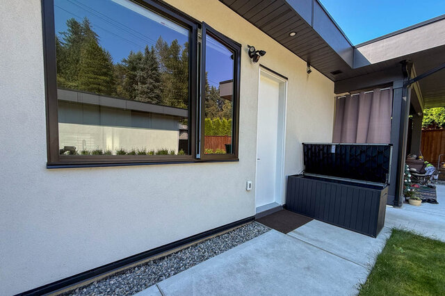Exterior entryway featuring a large framed window, white door, and concrete walkway bordered by gravel. - Suite-1384 Hope Road, North Vancouver