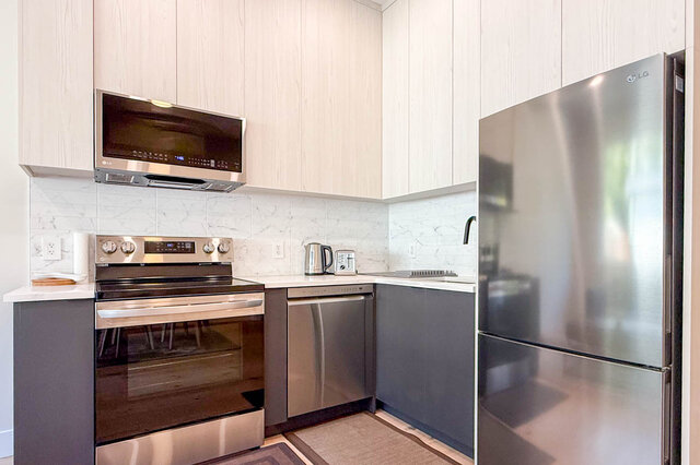 Modern kitchen with white marble countertops, light wood cabinets, and stainless steel appliances. - Suite-1384 Hope Road, North Vancouver