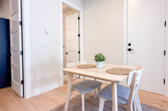 Compact dining nook with a light wood table, gray upholstered chairs, and pale hardwood floors. - Suite-1384 Hope Road, North Vancouver