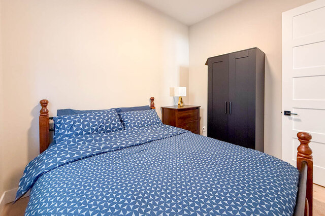 Cozy bedroom with a wooden four-poster bed dressed in blue patterned linens and a dark wardrobe. - Suite-1384 Hope Road, North Vancouver