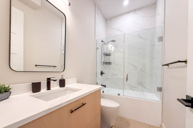 Bathroom with white marble countertops, a light wood vanity, and a glass-enclosed tub and shower. - Suite-1384 Hope Road, North Vancouver