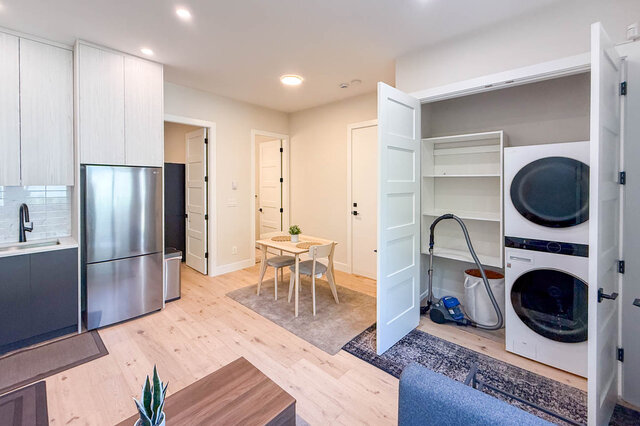 Open-plan living and dining area with light hardwood floors, stainless fridge, and a stacked washer-dryer nook.