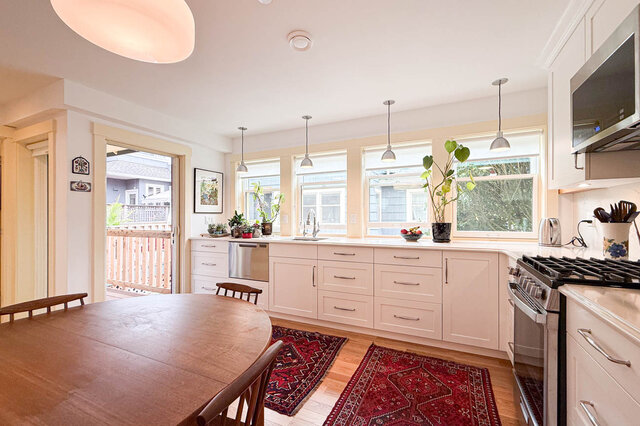 Bright kitchen and dining area with white cabinetry, hardwood floors, and red patterned rugs. - 3752 West 23rd Avenue, Vancouver West Side