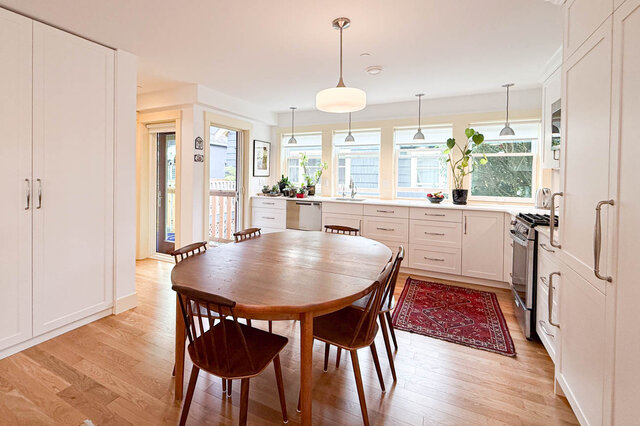 Bright kitchen-dining space with white cabinetry, hardwood floors, and a wooden oval table. - 3752 West 23rd Avenue, Vancouver West Side