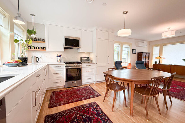 Bright open kitchen and dining area with white cabinets, marble countertops, hardwood floors, and a wooden table.