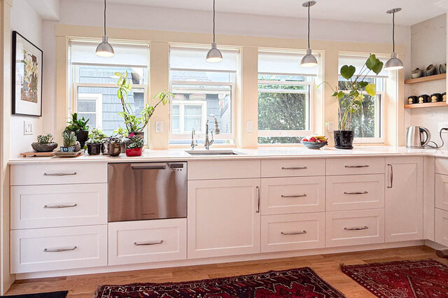 Bright kitchen with white shaker cabinets, stainless dishwasher, and hardwood floors beneath four windows.