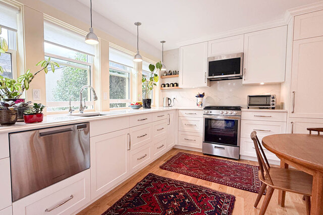 Bright kitchen with white shaker cabinets, stainless steel appliances, and red patterned rugs on hardwood floors.