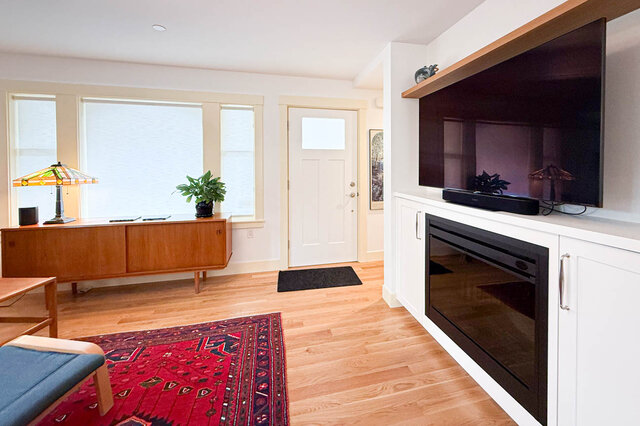 Living room with light hardwood floors, red patterned rug, and a wall-mounted TV above a fireplace. - 3752 West 23rd Avenue, Vancouver West Side