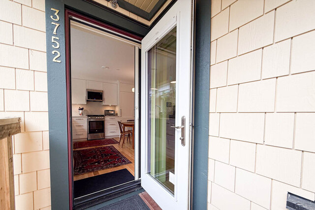 Kitchen with white cabinetry, stainless steel appliances, and hardwood floors seen through an open glass entry door.