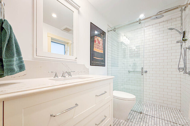 Bright bathroom with a white marble countertop vanity and a glass-enclosed walk-in shower in white subway tile.