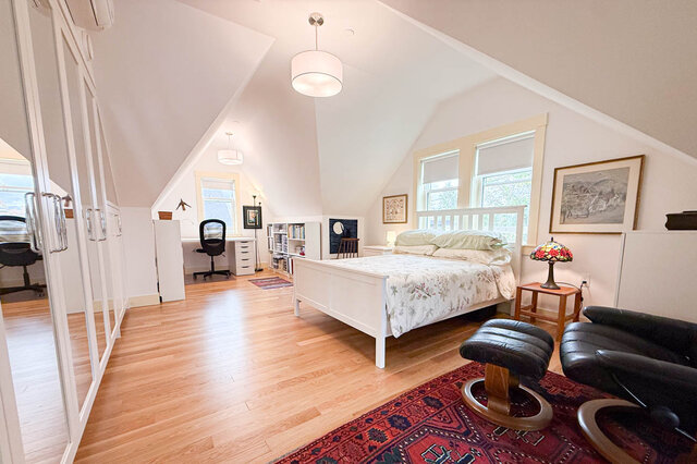 Bright bedroom with hardwood floors, a white bed, and a red patterned rug under a sloped ceiling. - 3752 West 23rd Avenue, Vancouver West Side
