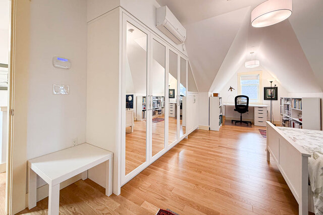 Bright attic bedroom with hardwood floors, mirrored closet doors, and a white bench under sloped ceilings.