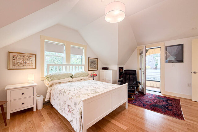 Furnished bedroom with sloped ceiling, white bed, hardwood floors, and a red patterned rug. - 3752 West 23rd Avenue, Vancouver West Side