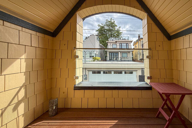 Attic loft with yellow shingle walls, vaulted ceiling, and an arched window framing a laneway view. - 3752 West 23rd Avenue, Vancouver West Side