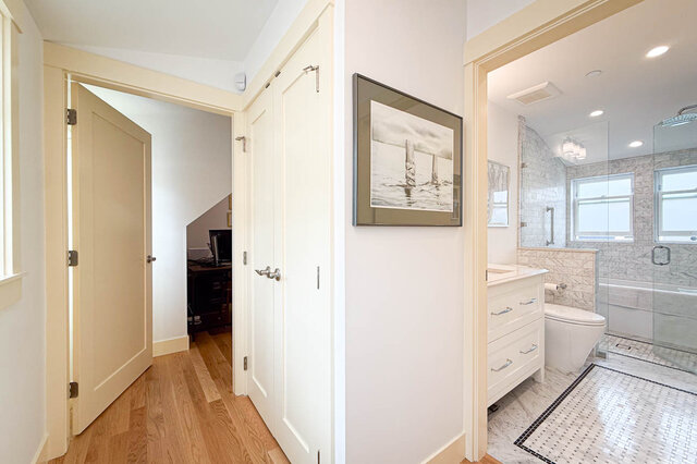 Hallway with hardwood floors and white closet doors opening to a bathroom with a glass shower and mosaic tile.
