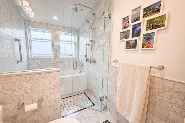 Elegant bathroom with white marble tile, glass-enclosed rain shower, and a gallery wall of framed photos. - 3752 West 23rd Avenue, Vancouver West Side